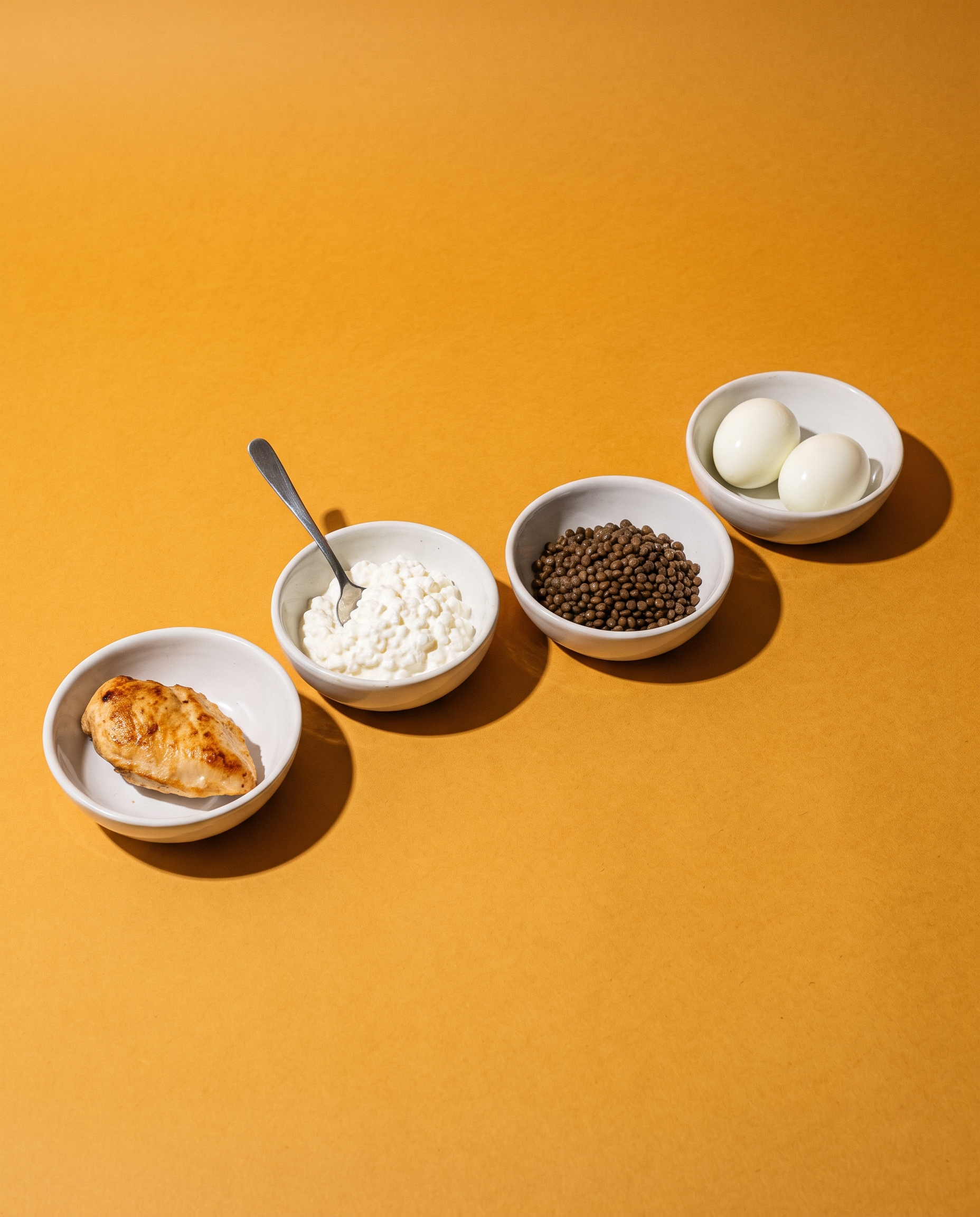 Four small white bowls of whole foods on amber paper, shot from above