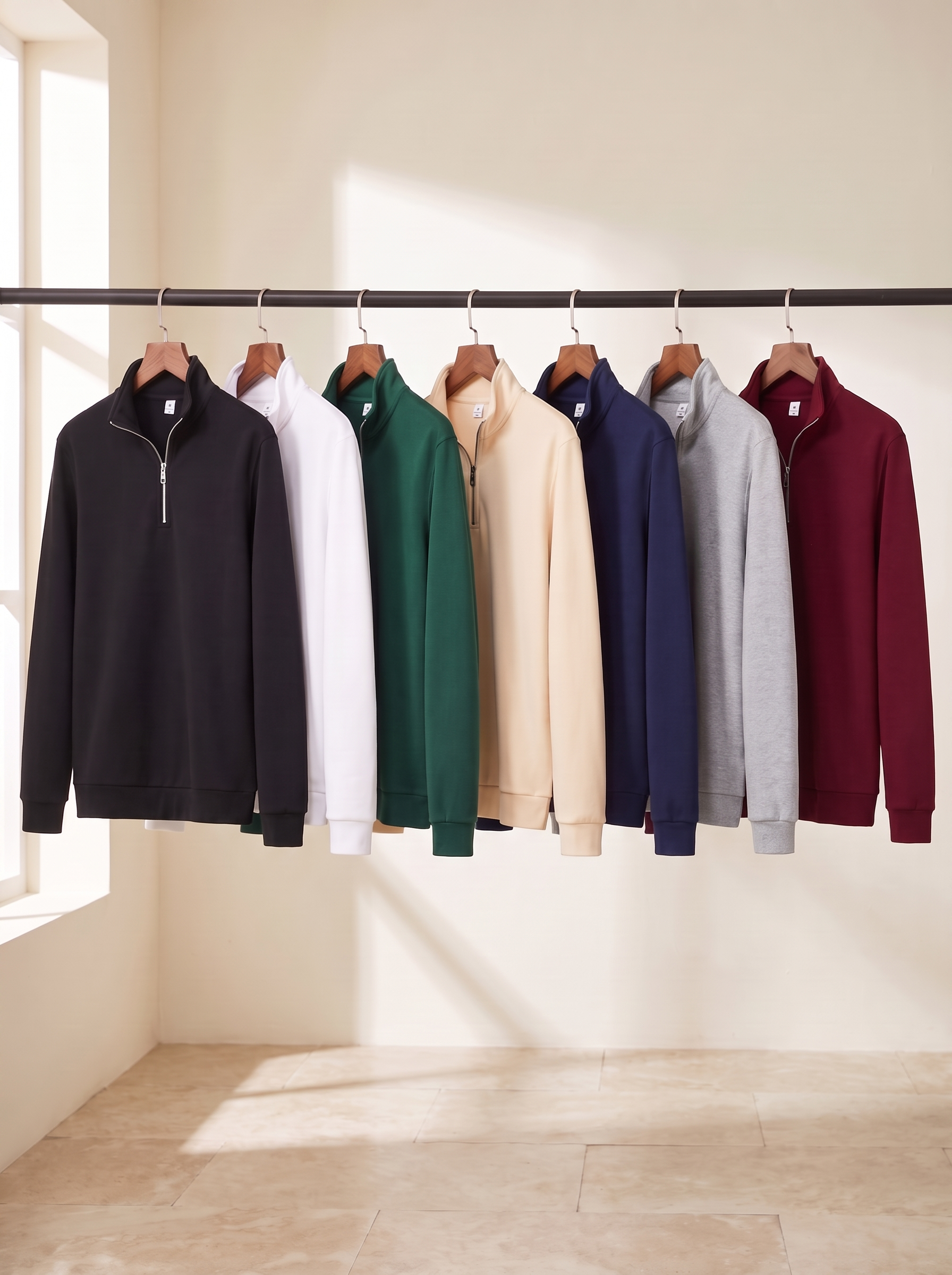 Sudaderas de media cremallera en siete colores sobre perchas de madera: negro, verde, azul marino, blanco, beige, gris y vino.
