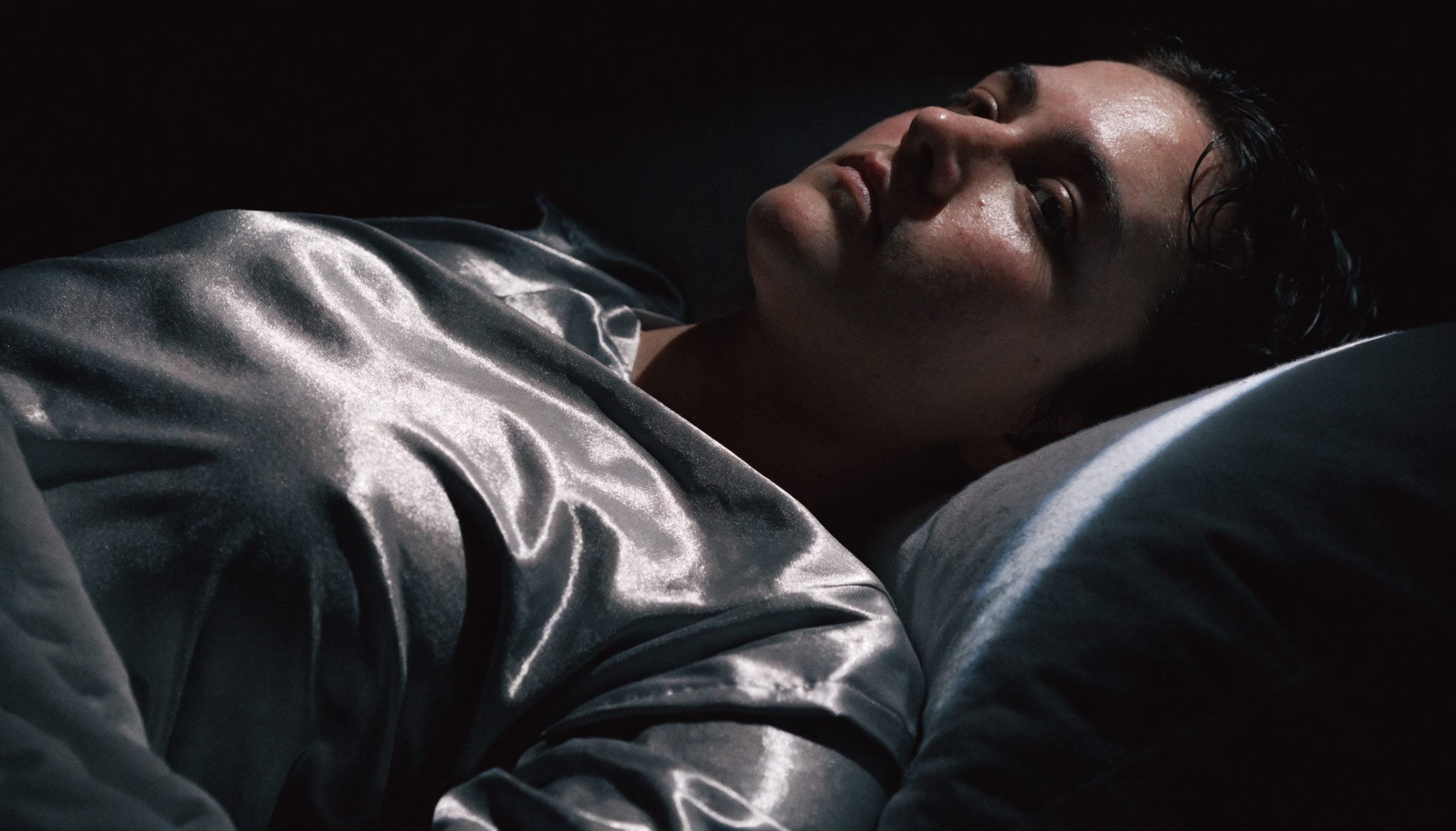 A person lying awake at night in a polyester satin pyjama shirt